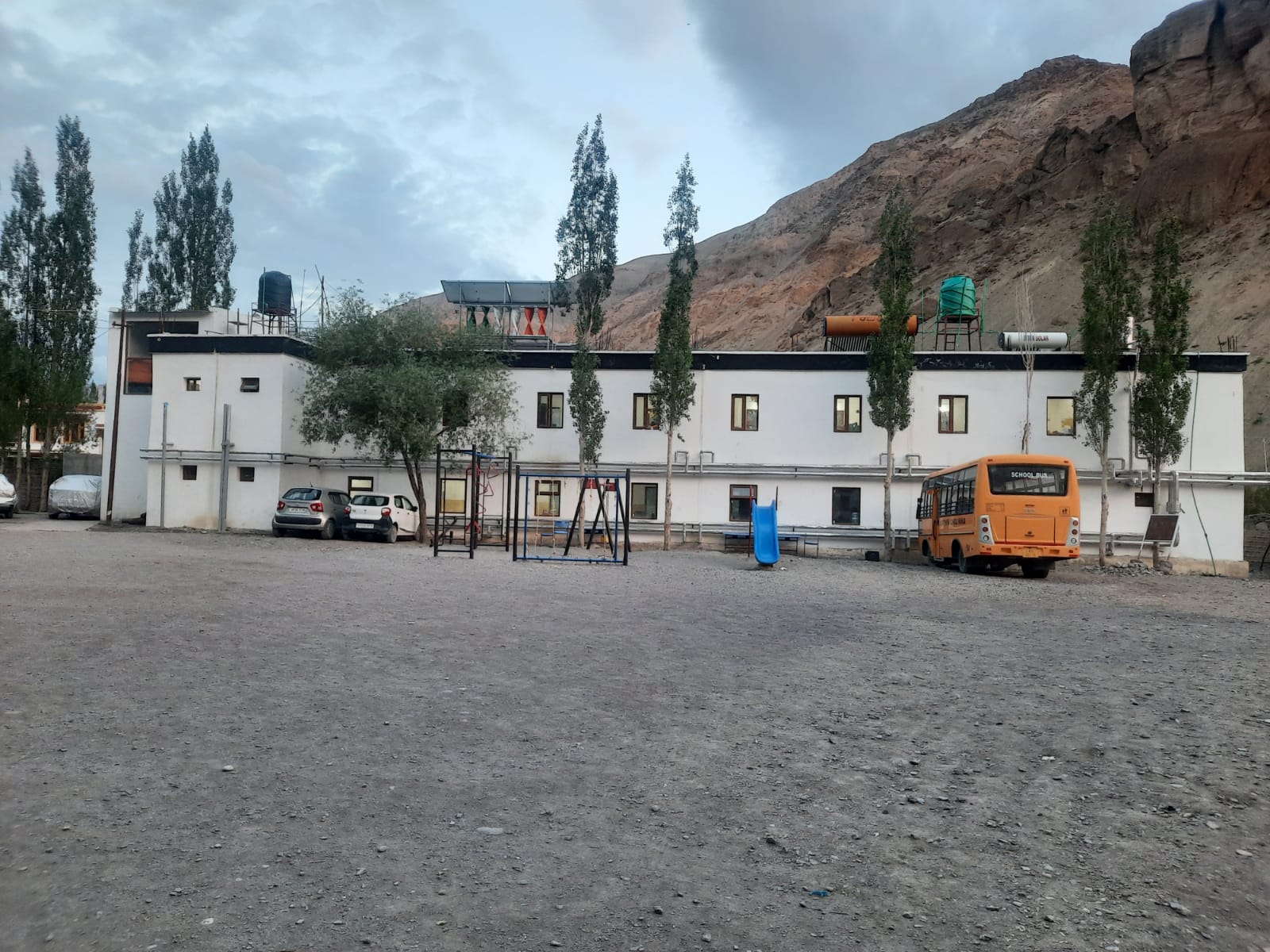 Open school playground with swings, slide and the school bus beside the school building