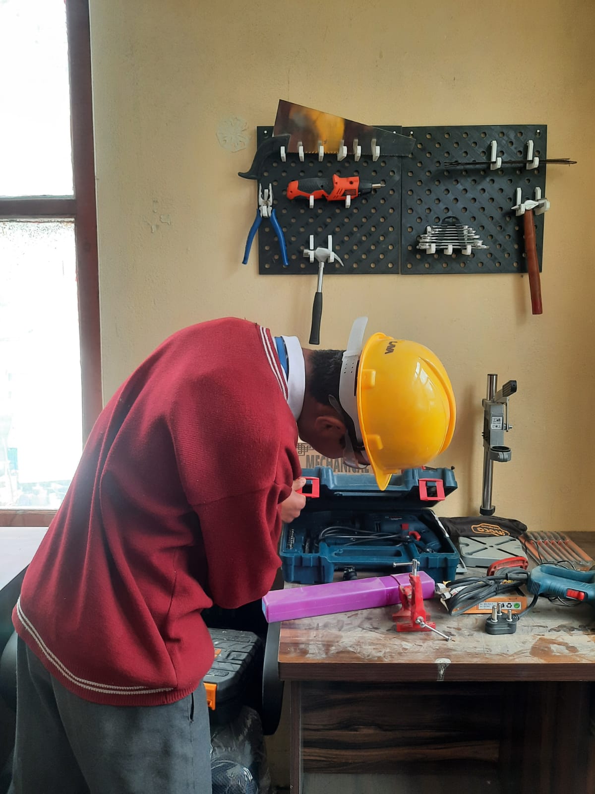 Student in a safety helmet working at the Atal Tinkering Lab workbench with tools