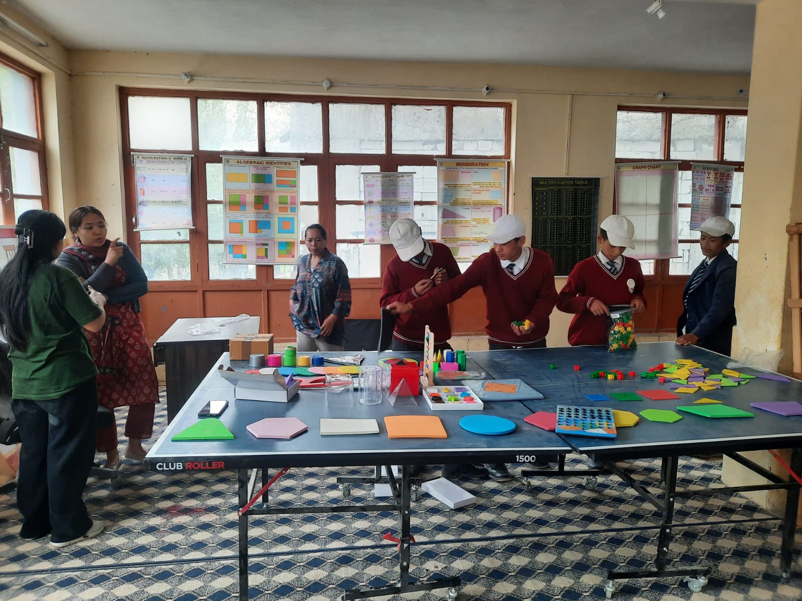 Students exploring geometric shapes and mathematics kits on a table in the maths lab